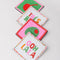 side stacked set of 4 beaded coasters: green beaded with cherry print, white with colorful beaded 'tres bien!', white with colorful beaded 'ooh lala', and pink with beaded olive.