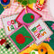 sideview of set of 4 beaded coasters: green beaded with cherry print, white with colorful beaded 'tres bien!', white with colorful beaded 'ooh lala', and pink with beaded olive on a colorful blanket