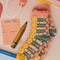 coral, teal, cream and yellow plaid chenille socks with coral ruffle top and cream grip bottoms on a pink background