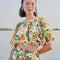 model wearing white cropped blouse with mixed fruit print and slight puff sleeves