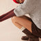 model wearing tall dark brown leather boots with silver buckle and strap detail around the ankle