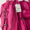 side view of raspberry pink leather tote bag with several zipper pockets, double handles, and crossbody strap