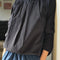 side view of model wearing black pin-tucked blouse with button neck opening