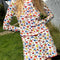 model wearing white cotton mini skirt with red lettuce trim, red bow front, and retro primary color floral print and matching cardi