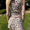 back view of model wearing white cotton mini skirt with red lettuce trim, red bow front, and retro primary color floral print