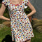 up close of model wearing white cotton mini dress with red lettuce trim, bow on the front bust, and retro primary color floral print