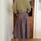back view of model wearing brown striped midi skirt with asymmetrical detail on the waist