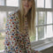 side view of model wearing white cotton cardigan with red lettuce trim, red button front, and retro primary color floral print