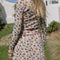 back view of model wearing white cotton cardigan with red lettuce trim, red button front, and retro primary color floral print