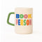 cream ceramic coffee mug with green handle and colorful 'book person' across the front and smiley face inside