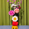 stacked vase with white flower, an apple on it's side and smiley face with flowers inside with flowers inside on a green and gingham background