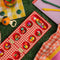 red and cream gingham mancala board with colorful fruit game pieces in grass