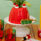 red jello mold vase/planter with a green plant inside on a stand surrounded by colorful kitchen items