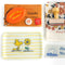 white tray with thin yellow stripes with woodstock smelling a yellow flower