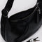 up close of zipper, buckle and interior key leash on model carrying black leather medium crescent bag