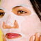 model with a white sheet face mask on their face