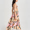 side view of model wearing pink midi dress with curved hem, corset bodice, and colorful abstract print