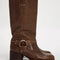 model wearing tall dark brown leather boots with silver buckle and strap detail around the ankle