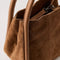 side view of cognac suede small handbag with piped handles