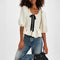 model wearing jacquard blouse with puff sleeves, slight peplum hem, and black bow and buttons on the bust