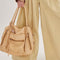 model carrying light tan leather purse with several zippered pockets, double handles and crossbody strap