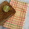folded cream tea towel with colorful thin plaid print with a cutting board and lime on it