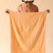 model holding light orange sand resistant beach towel with white line sketched banana leaf print and has white tassels at each end