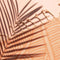 up close of light orange sand resistant beach towel with white line sketched banana leaf print and has white tassels at each end