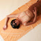 model laying on light orange sand resistant beach towel with white line sketched banana leaf print and has white tassels at each end
