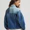 back view of model wearing patched denim chore jacket with a mix of light and dark wash denim and front patch pockets