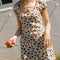model wearing white cotton mini dress with red lettuce trim, bow on the front bust, and retro primary color floral print