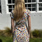 back view of model wearing white cotton mini dress with red lettuce trim, bow on the front bust, and retro primary color floral print