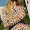 up close of model wearing white cotton cardigan with red lettuce trim, red button front, and retro primary color floral print