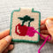 model creating tan needlepoint keychain kit with green trim and red and pink cherry print and gold hardware