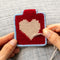 model creating red needlepoint keychain kit with baby blue trim, tan heart and gold hardware