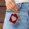 model holding red needlepoint keychain kit with baby blue trim, tan heart and gold hardware