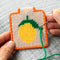 model creating tan needlepoint keychain kit with orange trim and lemon print and gold hardware