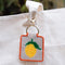 tan needlepoint keychain kit with orange trim and lemon print and gold hardware on a tote bag