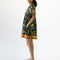 side view of model wearing navy blue babydoll dress with pin-tucked and large white button down the bust, with colorful fruit, baguette and leafy print