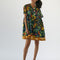 model wearing navy blue babydoll dress with pin-tucked and large white button down the bust, with colorful fruit, baguette and leafy print