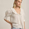 side view of model wearing ivory blouse with embroidered collar and hem, button front and pin-tucked details