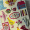 model showcasing cream embroidered journal wth various folk items - homes, butterflies, stamps, dog, cat, books