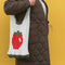 model wearing cream open knit market bag with red tomato in the middle and green trim