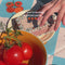 model setting up a tomato themed picnic with vintage themed bowls